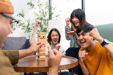 Happy asian diverse group friends playing with wooden building blocks at home office sitting at the table enjoying time together. Office leisure and board games concept.