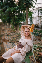Woman in light dress relaxing on the ground surrounded by greenery in a greenhouse