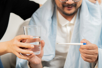Mature couple looking at thermometer checking temperature and holding glass of water at home.