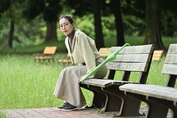 Fototapeta premium 雨傘を持ってベンチに座り微笑む日本人の女性