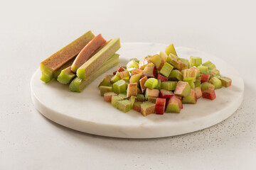 Freshly chopped green rhubarb on white chopping board on white table top. Trendy organic food. Ready for cooking. Vegan concept. Close up.