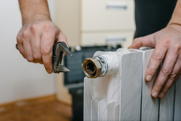 Closeup photo of man installing new heating radiator at home. Technician installing new heating radiator, unpacking and preparing for home heating setup