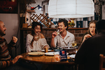 A group of friends laughing and sharing drinks and food around a cozy table indoors, showcasing warmth, joy, and camaraderie in a relaxed and friendly setting.