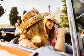 Two happy tourists wearing straw hats enjoying a ride in a convertible vintage car
