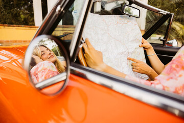 Two tourists consulting a map in a vintage convertible car during a road trip