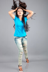 A young woman confidently poses wearing blue t-shirt, distressed denim jeans, heels, showcasing a casual urban style with charm and elegance, suitable for haircare, freedom, self-expression project