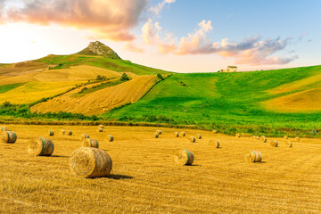 scenic agricultural landscape of summer season golden field with hay stacks during sunset or sunrise with green rural hills and beautiful mountains and clouds in evening sky on background © Yaroslav