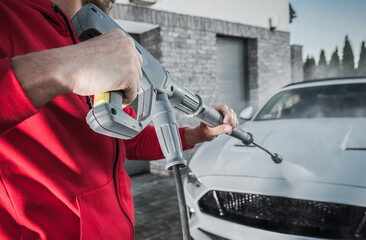 Man Using a Pressure Washer to Clean a Silver Sports Car at a Residential Garage in the Early Morning