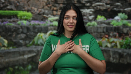 Volunteer woman in green shirt with tattoo gestures emotionally in outdoor park setting surrounded...