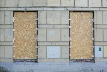 Two large windows in the wall of the building are covered with chipboard