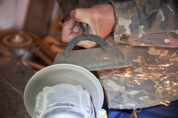 A man's hand sharpens a hoe on an electric sharpening machine in the village. Sparks from the...
