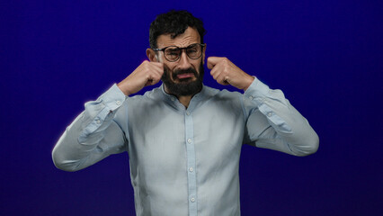 Man with beard appearing emotional, wearing glasses and light shirt against blue background using...