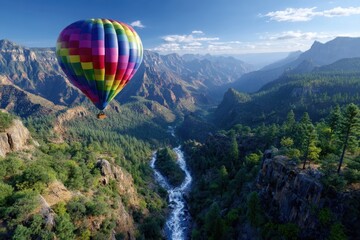 Fototapeta premium Colorful hot air balloon gliding over a rocky valley with a winding river and lush trees