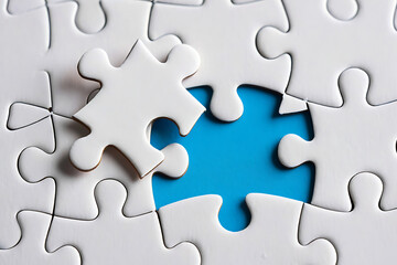 Fototapeta premium White puzzle pieces and the missing piece a conceptual symbol of completion and problem solving with a blue background