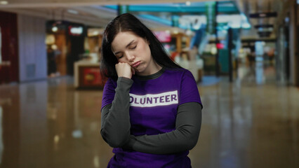 Woman in volunteer t-shirt looking tired in a mall environment, capturing the essence of community service dedication and fatigue.
