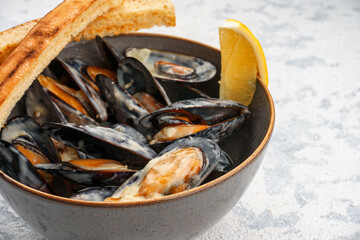 Mussels in Dor Blue sauce in a bowl with lemon and croutons, close-up.