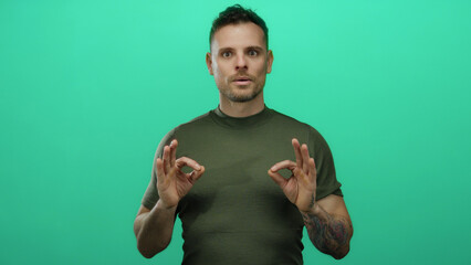 Young hispanic man meditating against isolated green background with calm expression and tattoos...