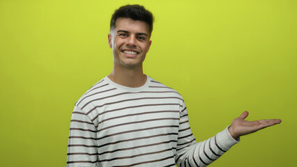 Young hispanic man smiling with open palm against isolated yellow background implying presentation...