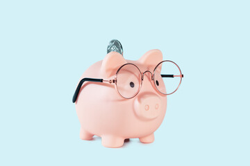 Pink piggy bank in glasses with coin isolated on blue background.