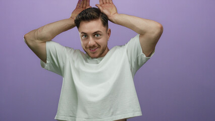 Young man with beard playfully posing against an isolated purple background with hands on head...