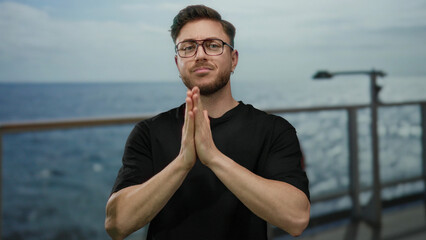 Fototapeta premium Young man with beard praying outdoors on a cruise ship against a seaside backdrop, embracing spirituality with eyes closed under the open sky on a boat journey at sea