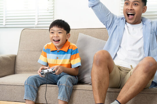 Joyful Family Moments and Gaming. A father and son share laughter during a gaming session in their cozy living room.