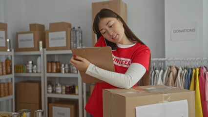 Woman volunteering at a charity center checks donations on a clipboard while talking on the phone,...