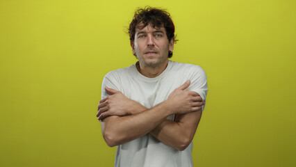 Hispanic man in white shirt shivering from cold against bright yellow background showcasing...