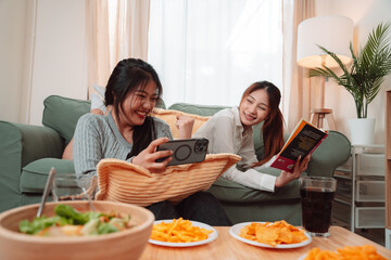 Asian Woman Friend Doing Lifestyle Indoor Smiling Phone Happiness, Sharing Joy and Memories Together at Home, Relaxing on Sofa with Smart Devices and Family Bonding Moments