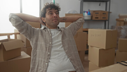 Hispanic man relaxing with a content smile amidst unpacked cardboard boxes in his new home,...