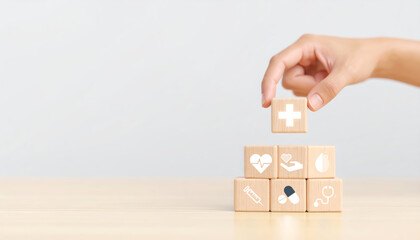 Hand stacking wooden blocks with medical icons including cross heart stethoscope and pills on light wooden table symbolizing healthcare wellness and medical support