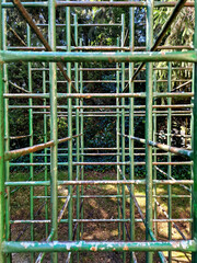 A view through an old green children's playground climbing frame in a wooded park during a sunny day