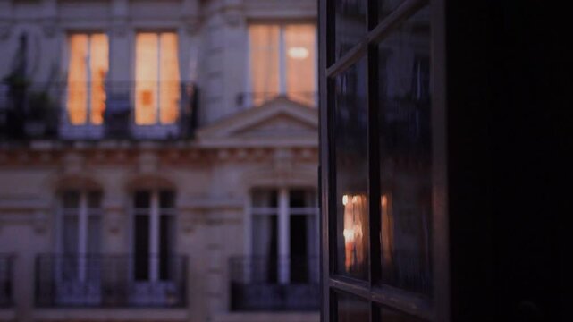 Warm lights reflecting on a window in a parisian building at dusk