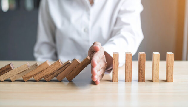 Person in white shirt stops falling wooden dominoes with their hand, symbolizing intervention, risk management, and prevention in business or personal context