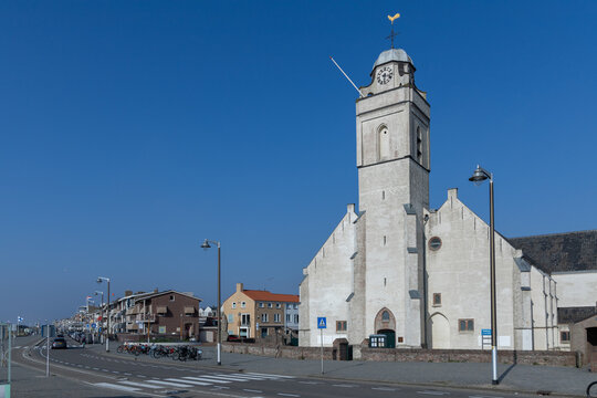 The prominent St. Andreas Church and its clock tower dominate the Katwijk aan Zee cityscape under a clear blue sky, with a street and buildings in the foreground.