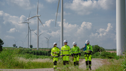 Maintenance engineer team standing at windmills at wind turbine farm. Group of people wear safety...