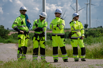 Maintenance engineer team standing at windmills at wind turbine farm. Group of people wear safety...