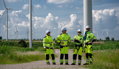 Maintenance engineer team standing at windmills at wind turbine farm. Group of people wear safety...
