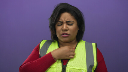 Hispanic woman in reflective vest appears tired and stressed against a purple background,...