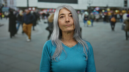 Grey-haired senior woman standing on a busy street in an urban outdoor setting, surrounded by...