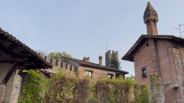 Medieval-style brick and stone buildings in Grazano Visconti, Italy, with towers, arched windows, and ornate details, captured under a clear blue sky