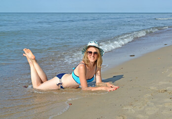 A joyful woman in a straw hat lies on the sand with her legs up. Baltic Sea. Kaliningrad region