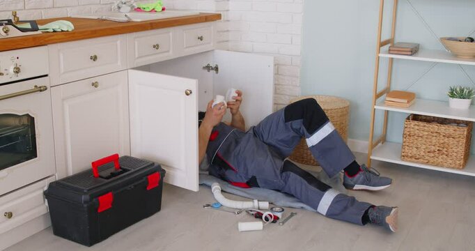 Plumber professional worker changes pipes under sink, fits and repairs fittings, water supply, sanitation, heating systems plumbing, sewage, installations, garbage disposal repair, drain cleaning 