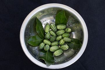 METAL COLANDER CONTAINING FRESH ORGANIC CUCA MELONS AND BAY LEAVES ON DARK BACKGROUND