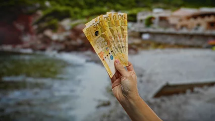 Gordijnen Hand holding philippine pesos outdoors by the seaside, depicting investment and business themes in a scenic town setting. © Krakenimages.com