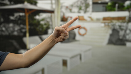 Man holding a victory sign with his hand on a sunny beach with lounge chairs and an umbrella in the background near the seaside.