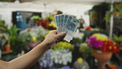 Man holding polish zloty banknotes in hand outside flower shop surrounded by colorful blossoms in vibrant market setting suggesting lively shopping environment.
