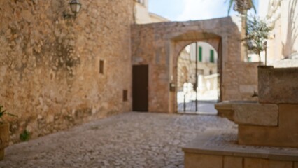 Blurred view of a historic campus cloister with stone walls and cobblestone path under sunny skies.