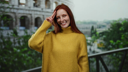 Woman smiling in yellow sweater with red hair standing outside roman coliseum on a sunny day in italy with greenery around creating a vibrant outdoor atmosphere.