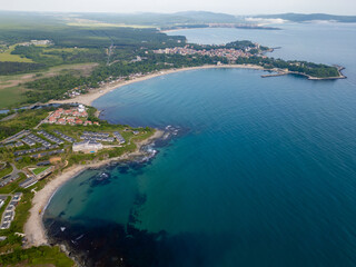 Aerial view of a scenic Bulgarian coastline with cliffs, turquoise water, sandy beaches, holiday homes, and green forest. Picturesque summer destination with modern resorts and nature
